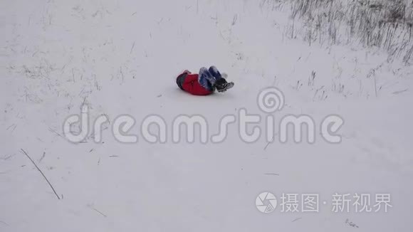 穿着红色夹克衫的快乐女孩在雪地里滑下山。 快乐的孩子在圣诞公园玩冬天。 慢慢