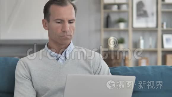中年男子坐在沙发上用笔记本电脑工作