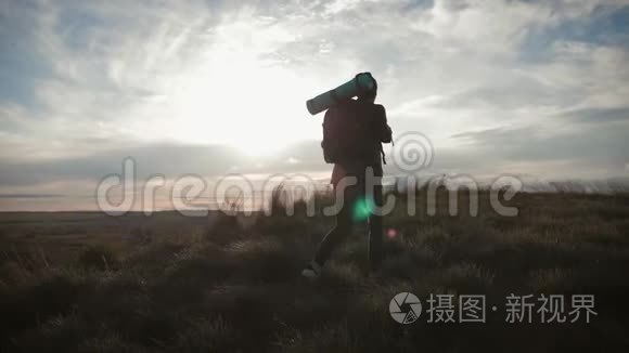 剪影年轻女孩带着背包，从山顶欣赏日落。 日落时分的游客。 人民