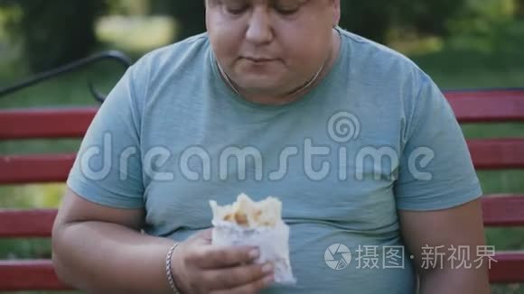 一个胖子在公园的长凳上吃有害的快餐，喝咖啡。