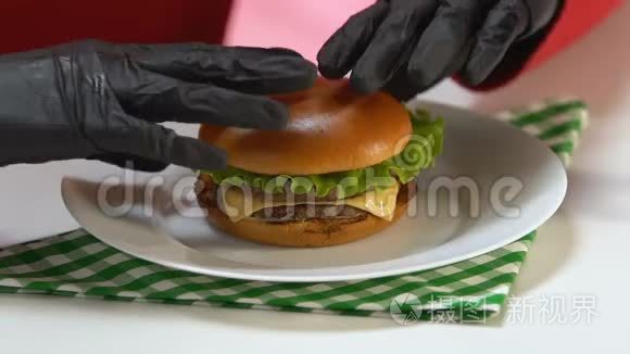 戴黑手套的人吃富含卡路里的快餐汉堡，暴饮暴食