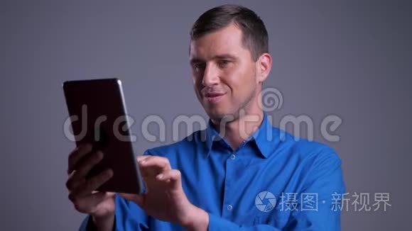 成人快乐白种人的特写肖像，他在平板电脑上轻敲，在镜头前微笑