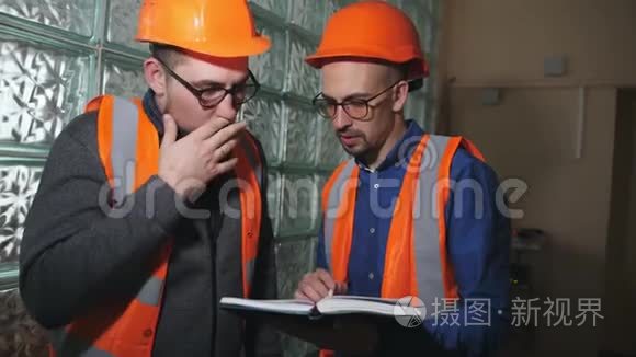 两名建筑工人在房间里戴着防护头盔，讨论建筑工程的计划。