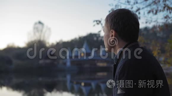 特写镜头，悲伤的男人在湖边的秋天公园喝茶