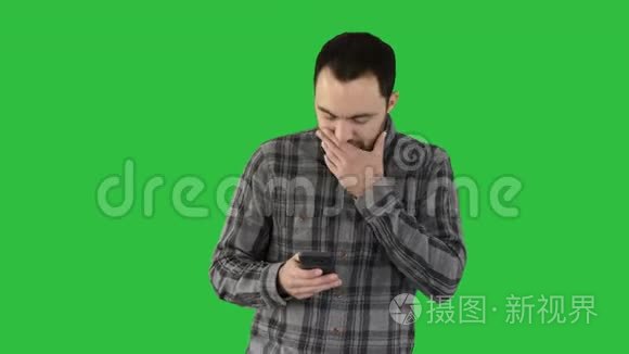 悲伤的年轻人走着，看着他的手机，他的手在他的脸上的绿色屏幕，Chroma键。