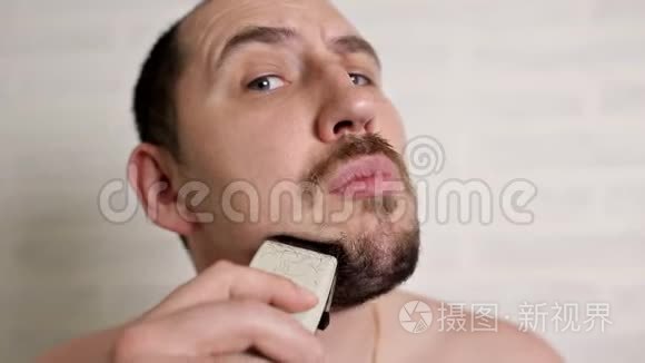 一个人用电动剃须刀刮大胡子。 一个人的特写肖像