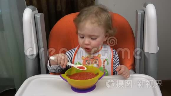 一个穿背心和围兜的孩子在一碗汤里拿着勺子