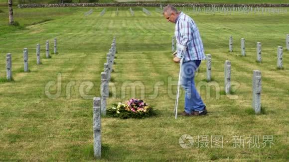 残疾老兵拄着拐杖在墓边修花