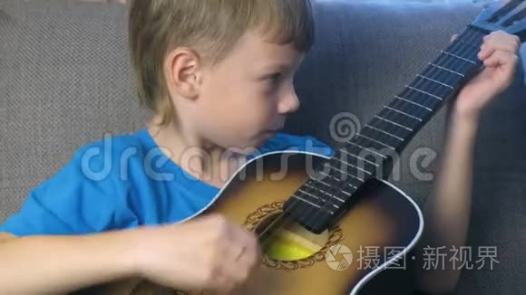 男孩学会坐在沙发上弹吉他。 学习演奏乐器的概念..