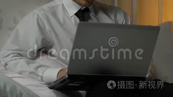 疲惫的男性晚上在笔记本电脑上工作，坐在酒店房间里，出差
