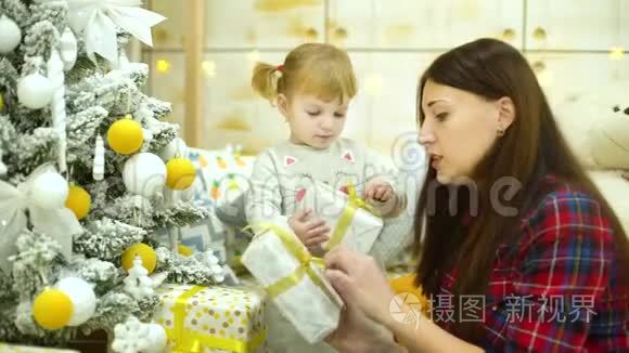 可爱的小女孩和年轻的母亲在家附近的圣诞树旁打开礼物盒