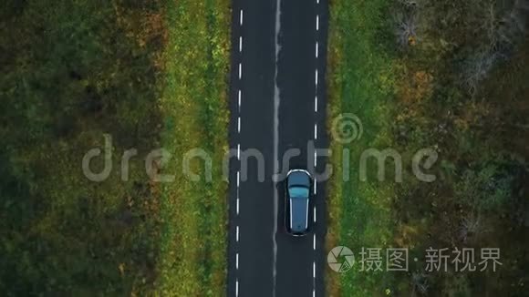 顶视图摄像机跟踪黑色汽车行驶在空高速公路上，沿着多云的秋林进行大气道路旅行。