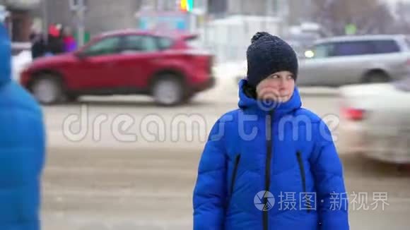 穿着蓝色羽绒服的少年站在街上。 汽车在后台行驶，男孩环顾四周。