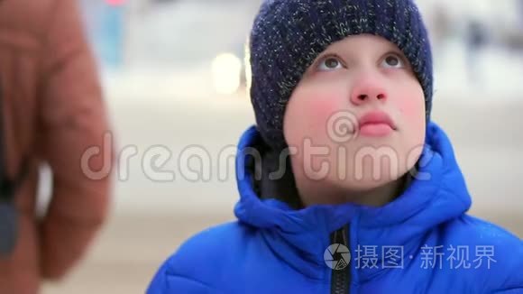 穿着蓝色羽绒服的少年站在街上。 汽车在后台行驶，男孩环顾四周。