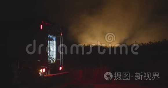 开着闪烁灯的消防车。 森林火灾时在野外焚烧草地背景下的消防车。 救援和救援