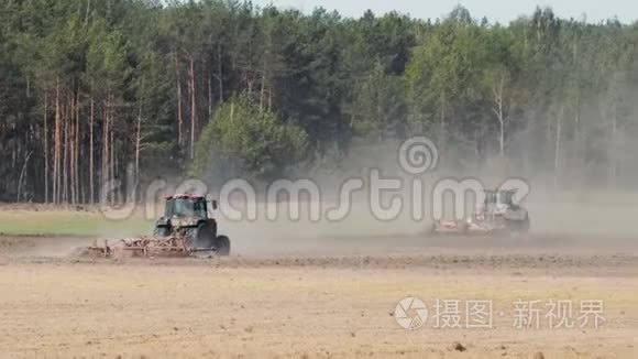 两台强力拖拉机在针叶林背景下，在炎热的阳光天气下耕作干燥的土壤