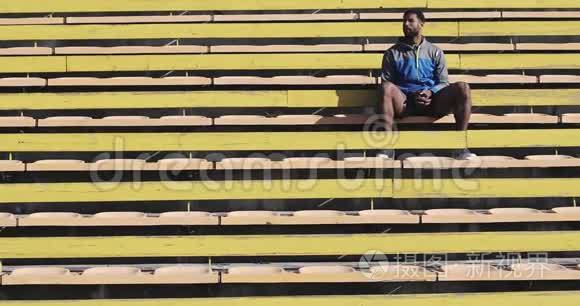 一位黑人男性运动员坐在体育场的黄色楼梯上。