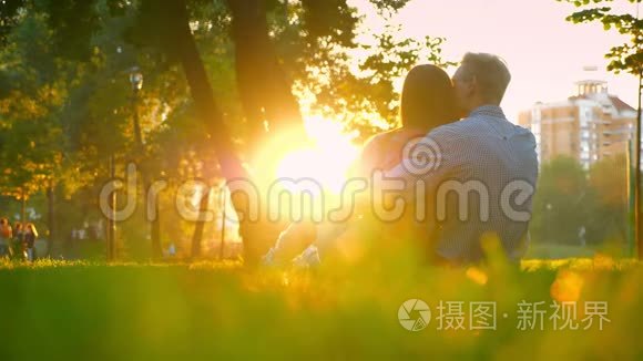 两个女人和一个男人在公园里坐在一起，互相拥抱，当太阳照耀着他们的轮廓和轮廓时。