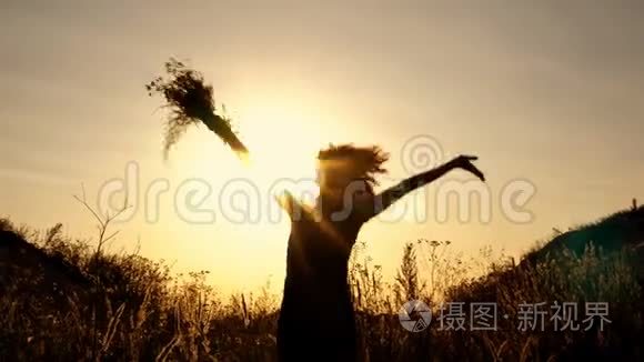 一个女孩在灿烂的夕阳背景下的黑色剪影。 她跳起来，在花丛中挥动双手