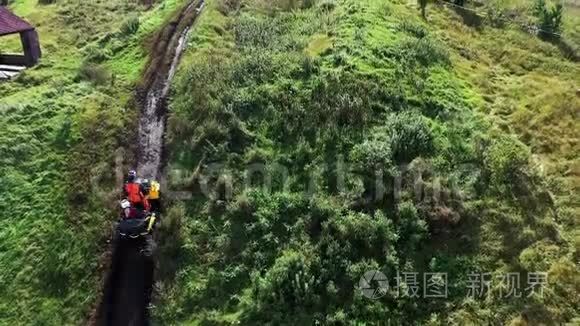 在绿色草地上泥泞的小径上，骑着四轮摩托车的赛车在农村的空中俯视。 股票