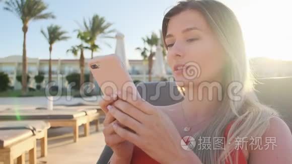 女性使用智能手机在躺椅上休息的肖像，浏览互联网，通过社交媒体滚动。 青年