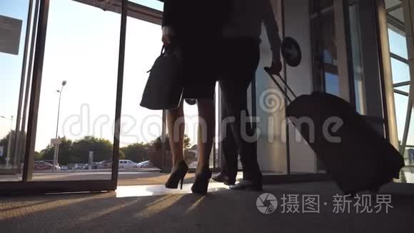 商务人士带着行李通过自动玻璃门离开机场。 年轻男女穿着高跟鞋走路