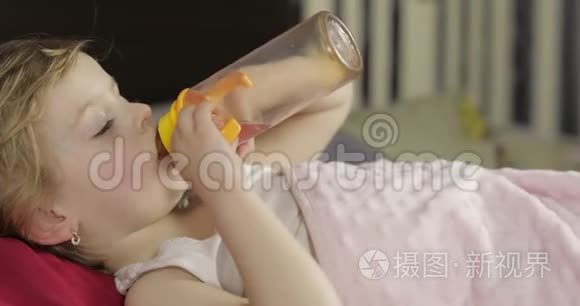 可爱的女婴睡在家里舒适的床上，喝着瓶子里的果汁