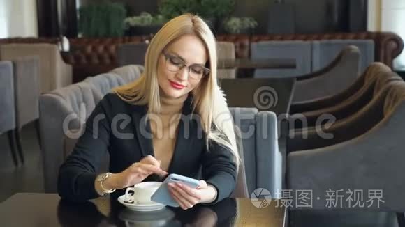 一个穿着西装，拿着电话坐在咖啡馆里的餐桌旁的漂亮女商人