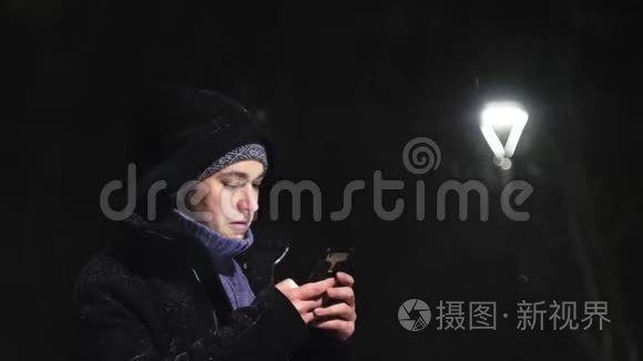 街灯里的那个人。 那家伙看着他的智能手机。 `在灯的背景下下雪。 慢动作