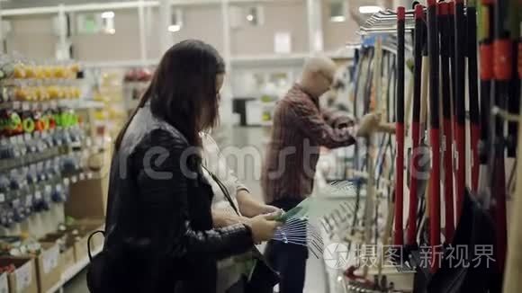 一对老年夫妇和成年女儿在五金超市选择耙