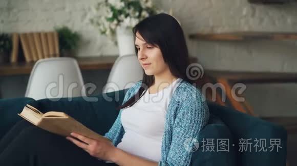 平静的女孩正坐在家里的沙发上看书，翻开书页，享受和平文学和舒适。 不错的阁楼风格