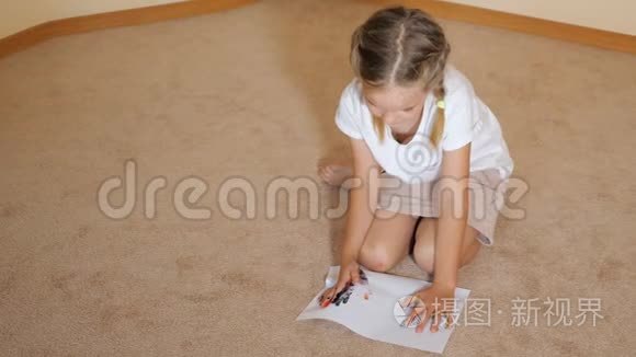 小女孩坐在地上拿着纸，在家里拿着水彩画画