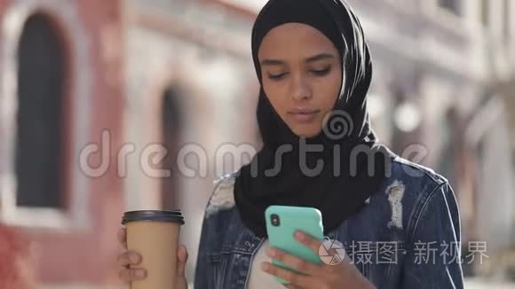 年轻的穆斯林妇女戴着头巾在市中心散步，使用智能手机和喝咖啡