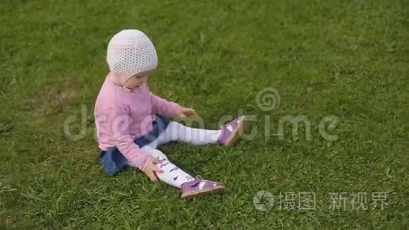 一个夏天，戴着帽子的两岁小女孩坐在绿草上。