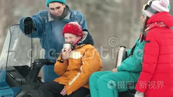 一家人坐在雪地摩托上，在森林里喝茶