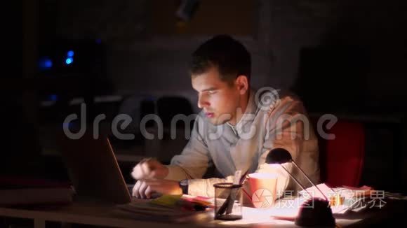 漂亮的高加索人正在笔记本电脑上打字，用巨大的哈欠精确地看着屏幕，在黑暗的办公室里，lante时间