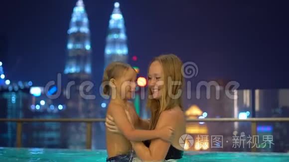 一位美丽的年轻女子和她的小儿子在屋顶的游泳池里玩得很开心，可以看到摩天大楼。 前往亚洲