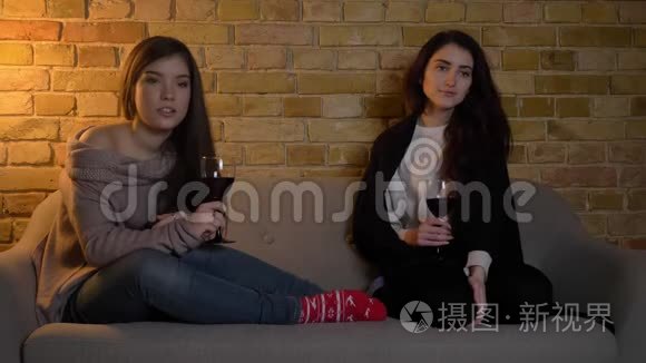 年轻的白种人女性朋友坐在沙发上，端着酒杯，在舒适的家里看电影