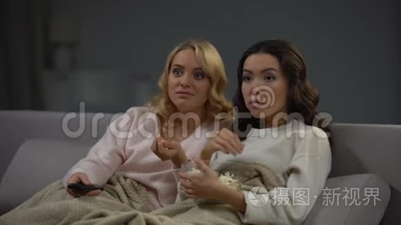 两个震惊的女人吃爆米花，看有趣的电视节目，休息