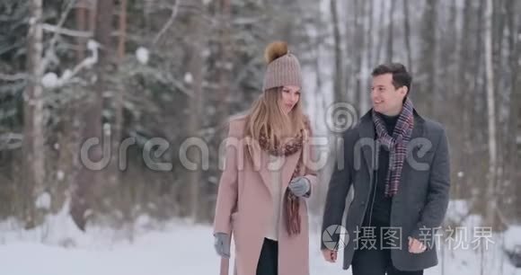 年轻的夫妇走过冬天的森林。 一男一女看着对方，笑得很慢