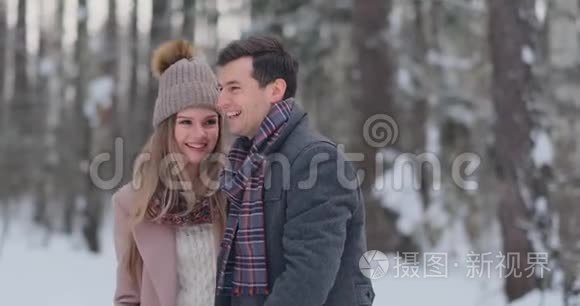 年轻的夫妇走过冬天的森林。 一男一女看着对方，笑得很慢