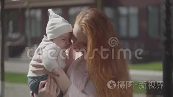 一位年轻可爱的红发妈妈抱着一个可爱的孩子在春天阳光明媚的时候和他说话