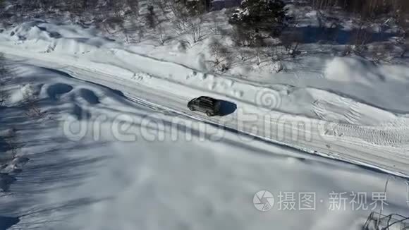 在一个阳光明媚的日子里，黑色的面包车正在一条覆盖着雪的道路上行驶，在4k的空中拍摄