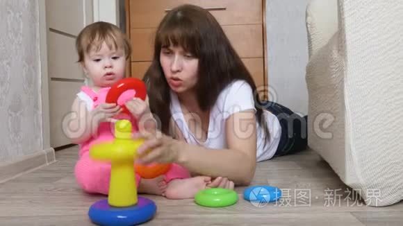 妈妈和小女儿玩五颜六色的戒指，他们在孩子们地板上的房间里收集玩具金字塔