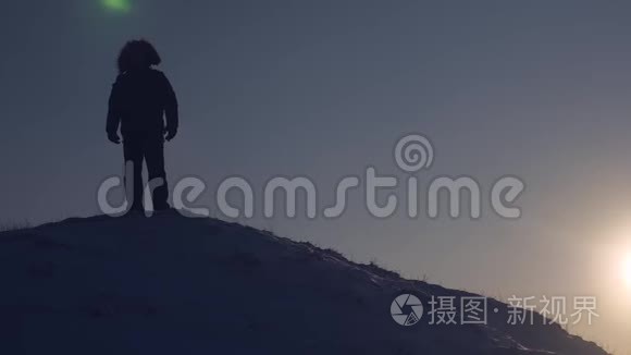 在明亮的日落下，一位游客站在山上。旅行时自然条件寒冷。征服