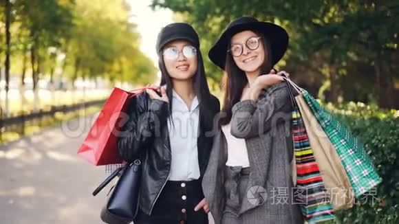 美丽的年轻女性购物者站在街上，拿着纸袋，微笑着看着相机的画像