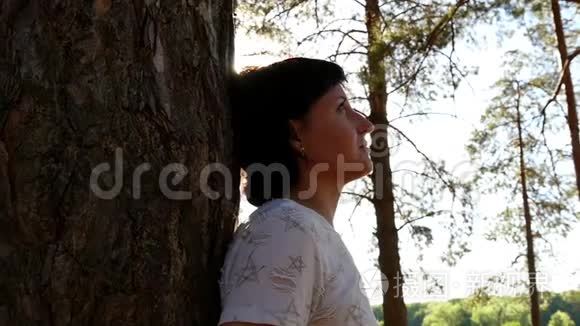 一个小女孩站在森林里的一棵树旁。运动摄影机滑块。在树林里休息，在新鲜空气中散步。