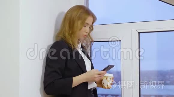 公司女经理在智能手机上发短信，并在窗户附近端着一次性咖啡