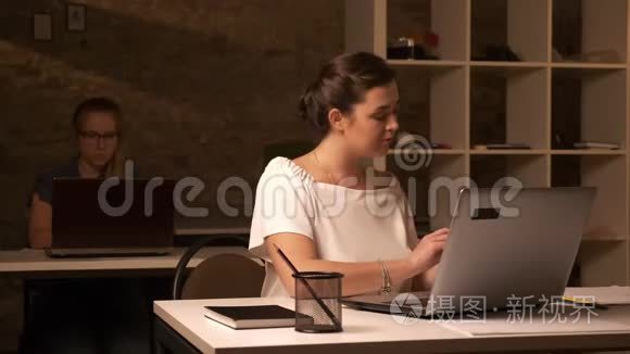 一位严肃的白种人女商人正在看着她的电脑和工作场所的人进行电话交谈