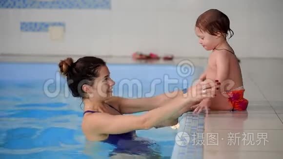 在游泳池里，婴儿从旁边跳到水里，慢慢地游向母亲